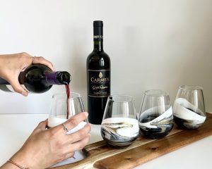 hands pouring red wine into one of 4 beautifully hand decorated glasses
